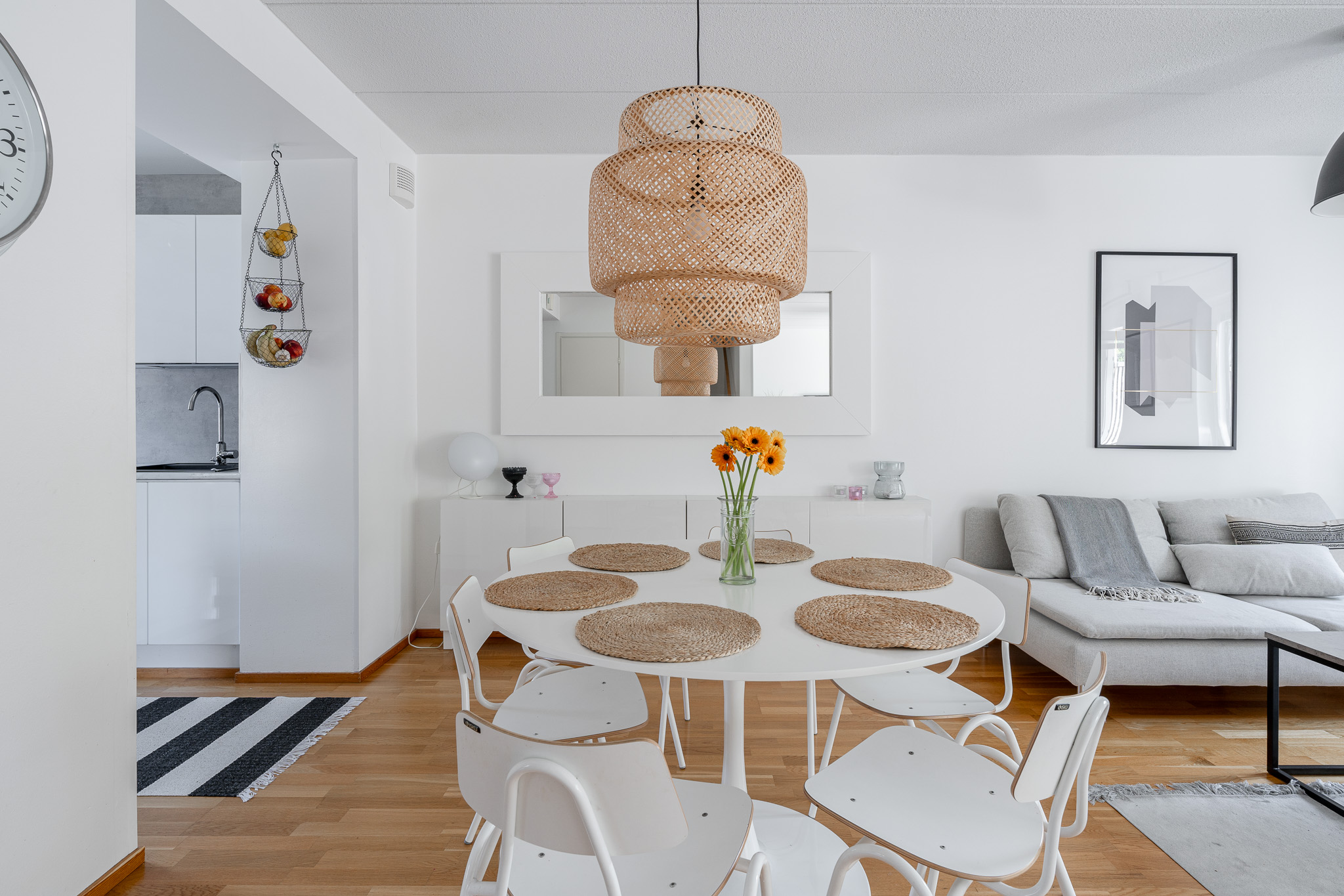 Bright open living and dining area with a round white table, rattan pendant and linen sofa